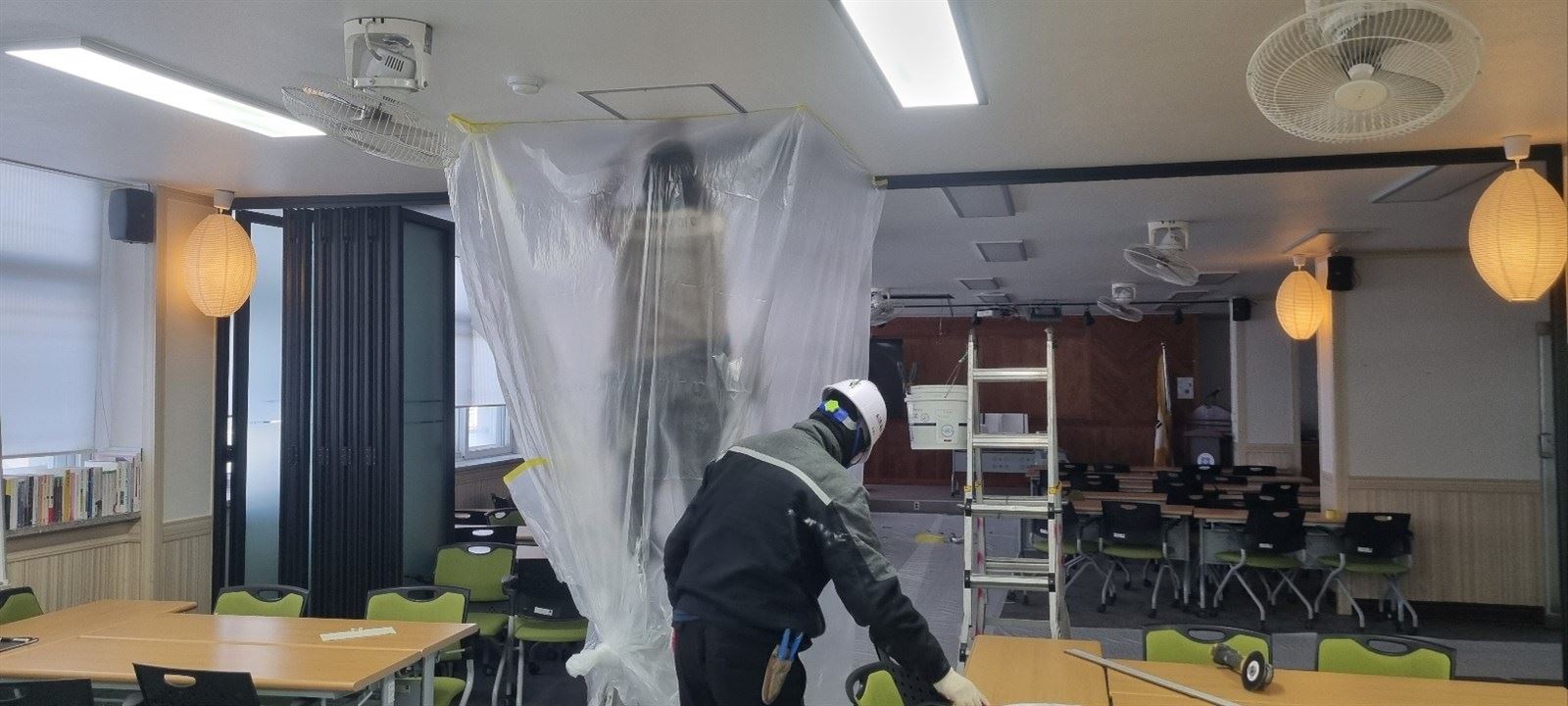 천장 작업 구역을 비닐로 둘러싸고 안전모를 쓴 작업자가 작업하는 모습